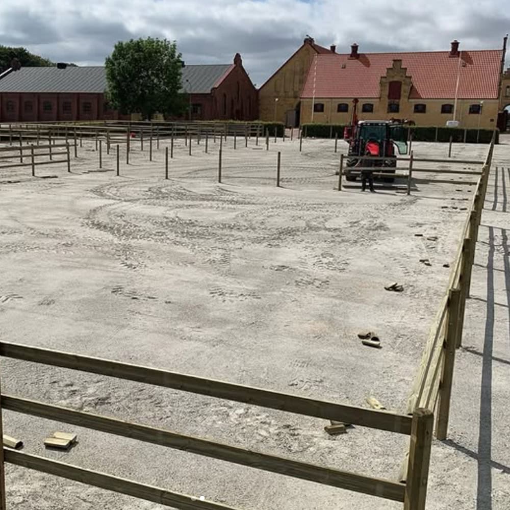 Häststängsel och byggarbetsplats på gård med lantliga byggnader i bakgrunden.