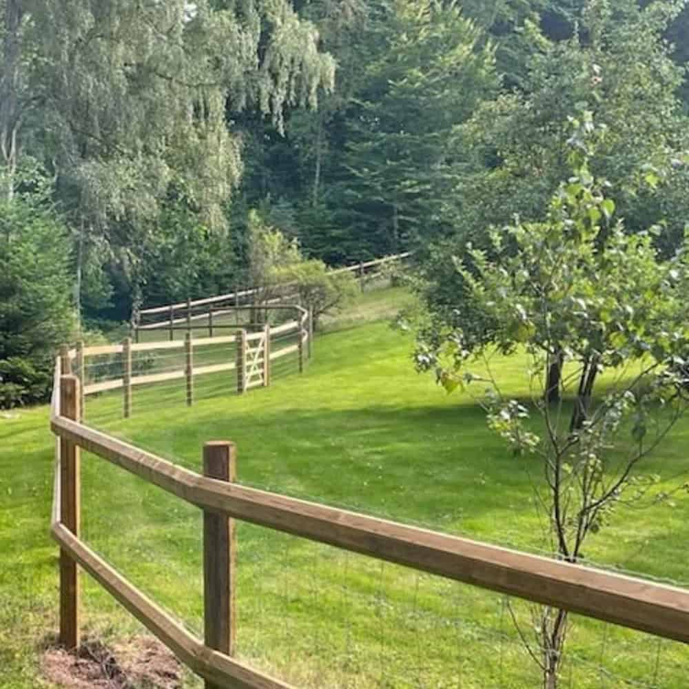 Trästängsel för häststängsel i naturskön miljö med gröna gräsmattor och träd.